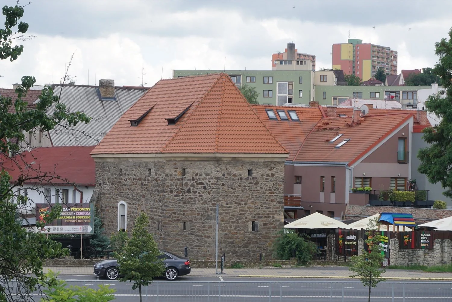Husitská bašta v Bílině z odstupu přes silnici, v pozadí panelák