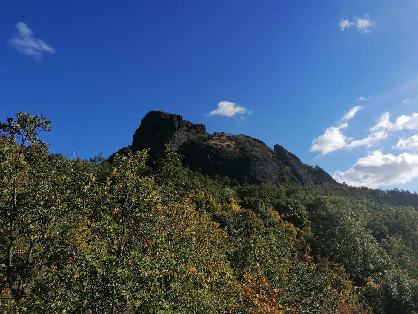 Skalnatý vrchol Bořeně nad lesem s podzimním listím pod modrou oblohou