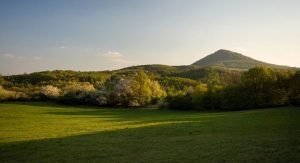 Milešovka: Pohled na horu Milešovku, louka, lesy a modrá obloha.